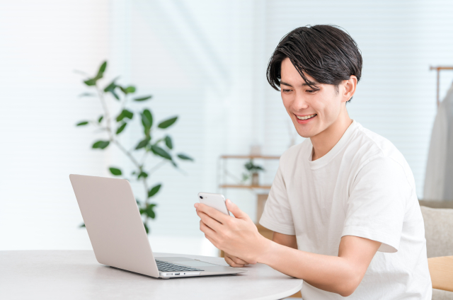 永住許可申請を考える外国人会社員がパソコンとスマートフォンで副業をしている様子